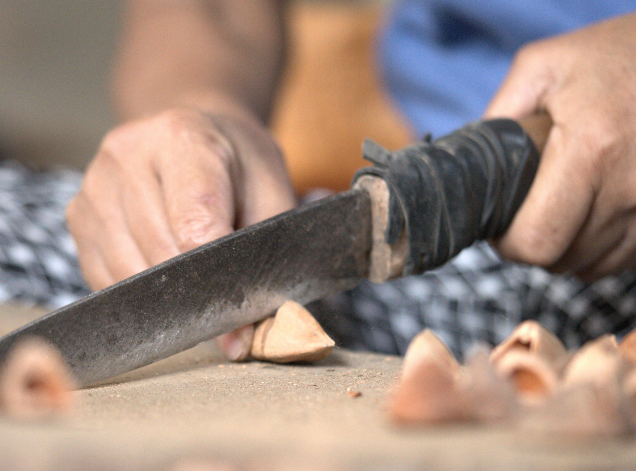 Close-up of a Filipino farmer's hands cracking open a pili nut with a bolo knife on a wooden block, showing traditional pagtilad harvesting technique.