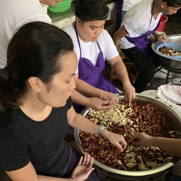 Chef Rica Dakudao Buenaflor and local farmers sorting pili nuts together at a processing facility in Sorsogon, Philippines.