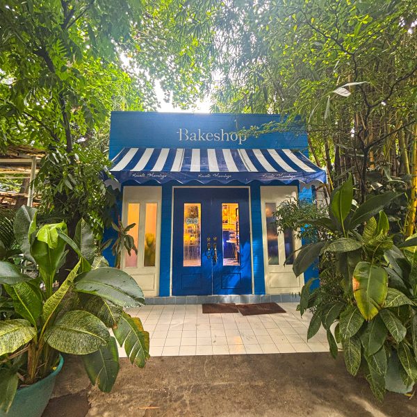 Interior of Rustic Mornings Bake Shop showing vintage-style shelving, chalkboard signs, and baked goods like sourdough, truffle ensaymadas, and lemon loaves in a cozy, homey setup.
