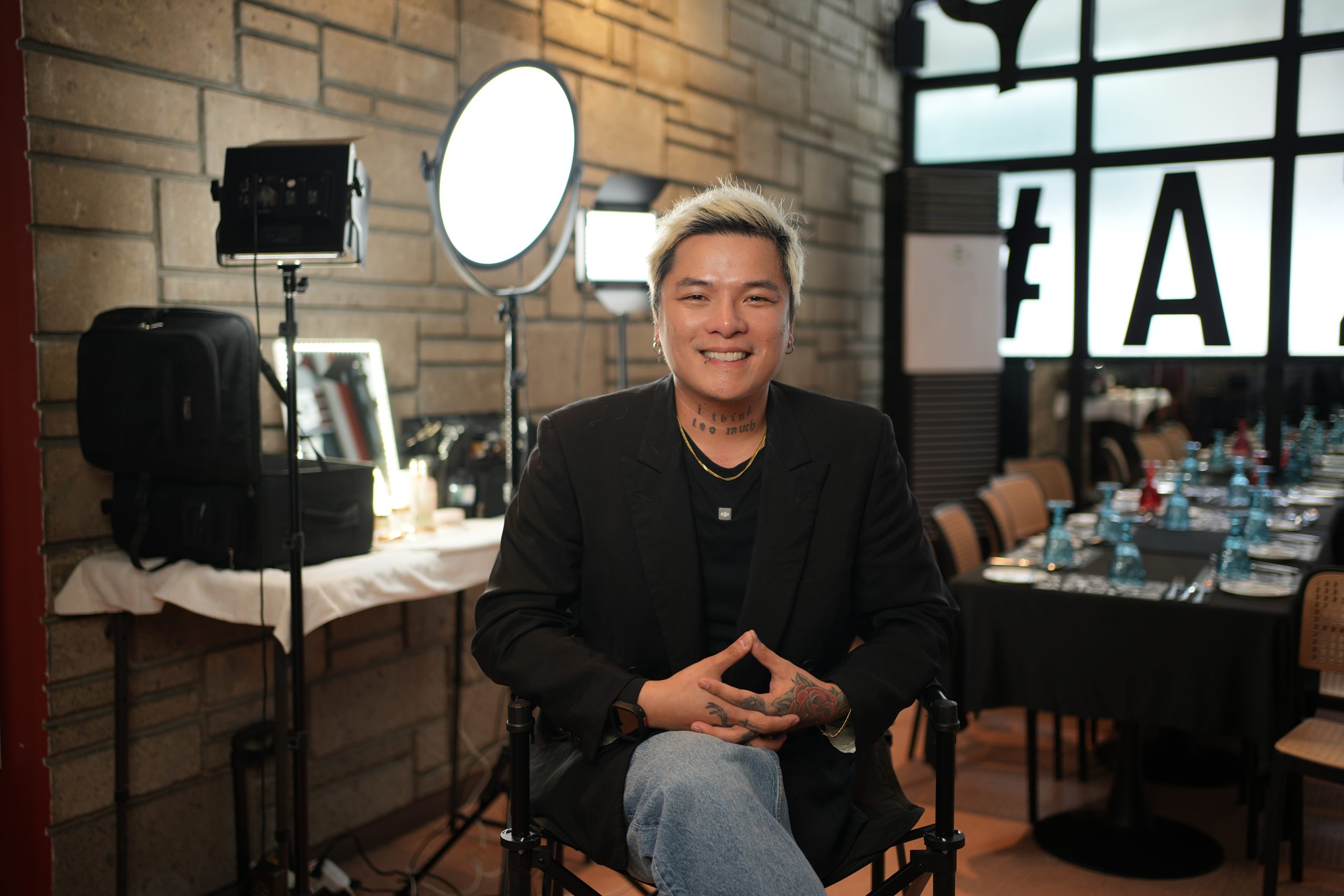 Makeup artist Cairo Manta smiling during a bridal makeup demo, wearing a black shirt, surrounded by natural light and soft glam tools