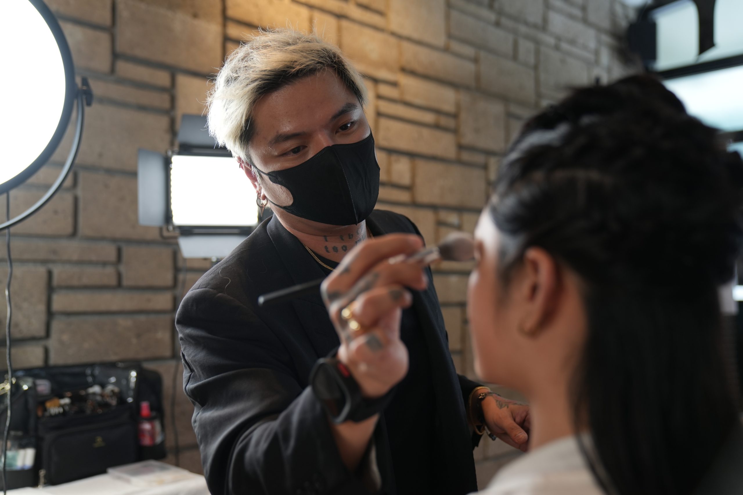 Makeup artist Cairo Manta applying bronzer on a Filipina bride during a soft glam demo, surrounded by tools and natural light