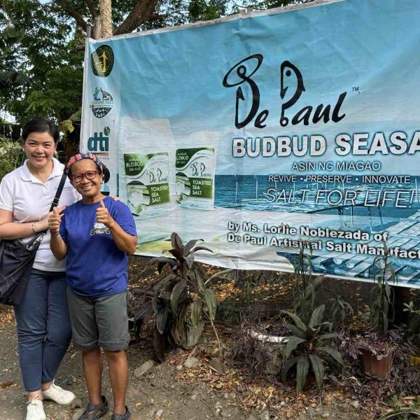 Author and Lorlie Paguntalan Noblezada posing outside the De Paul salt facility in Miag-ao, with the workshop tarpaulin in the background, home of Miag-ao artisanal sea salt.