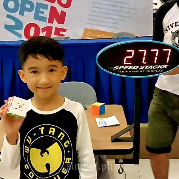 Young Leo Borromeo smiling at his first Rubik’s Cube competition, holding a timer and puzzle in hand.